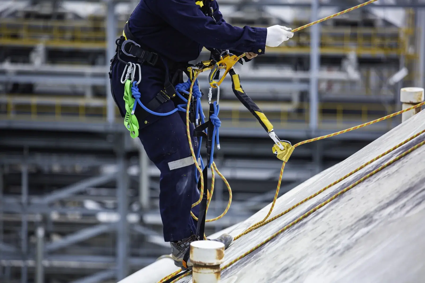 Cable de acero inoxidable tensado sobre una cubierta metálica con postes intermedios y absorbedor de energía en el extremo, y un operario enganchado con arnés de cuerpo completo